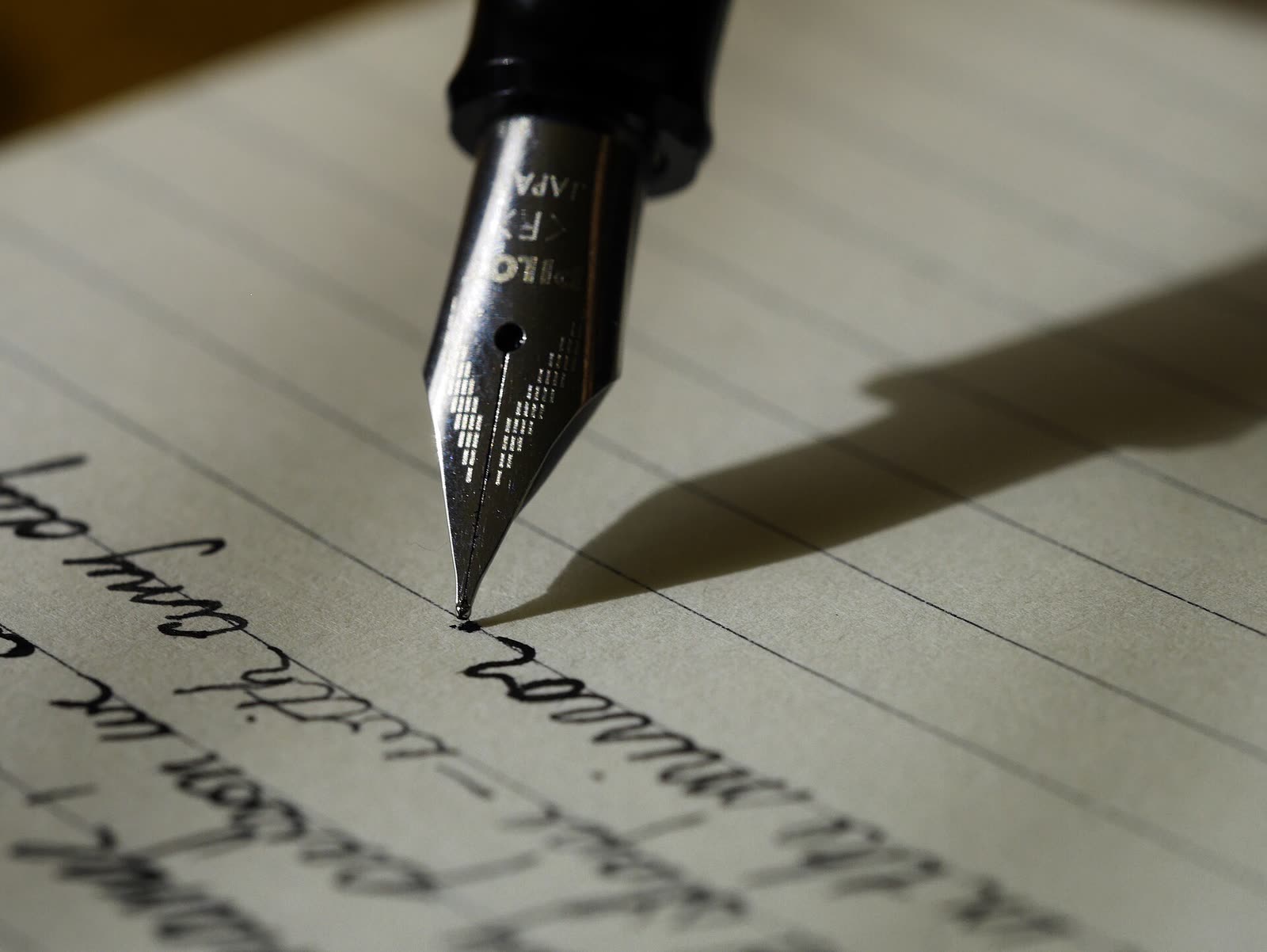 Punta de una pluma estilográfica escribiendo a mano sobre un papel rayado, iluminada de lado